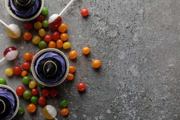 Draufsicht auf köstliche Halloween-Cupcakes, Lutscher und Bonbons auf betongrauer Oberfläche — Stockfoto