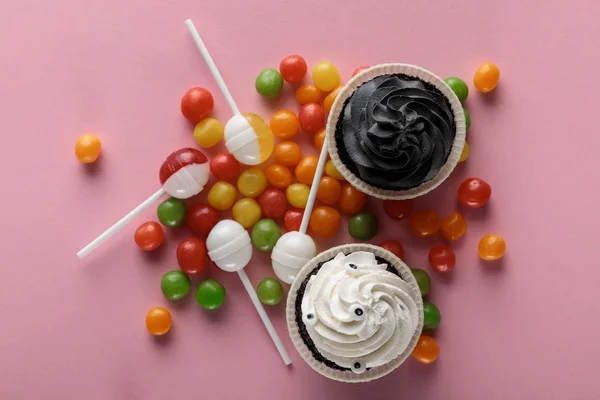 Draufsicht auf köstliche Halloween-Cupcakes, Lutscher und Bonbons auf rosa Hintergrund — Stockfoto