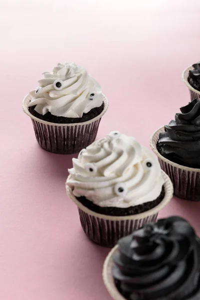 Deliciosos cupcakes de Halloween com creme branco e preto no fundo rosa — Fotografia de Stock