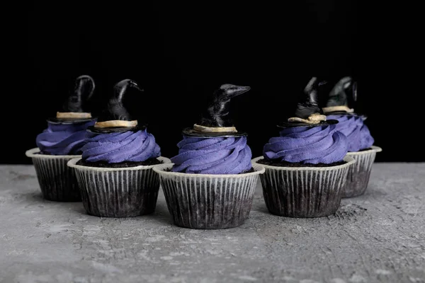 Cupcake di Halloween con crema blu e cappelli decorativi da strega su superficie grigio cemento isolato su nero — Foto stock