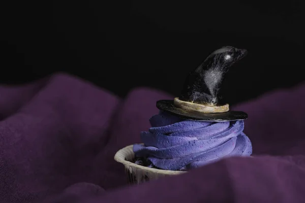 Savoureux cupcake d'Halloween avec crème bleue et chapeau de sorcière décoratif sur tissu violet isolé sur noir — Photo de stock