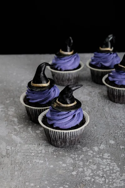 Sabrosos cupcakes de Halloween con crema azul y sombreros de brujas decorativos en la superficie gris de hormigón aislado en negro - foto de stock