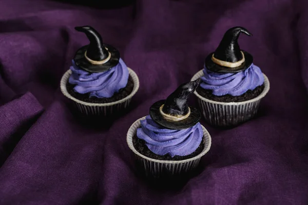 Tasty Halloween cupcakes with blue cream and decorative witch hats on purple cloth — Stock Photo