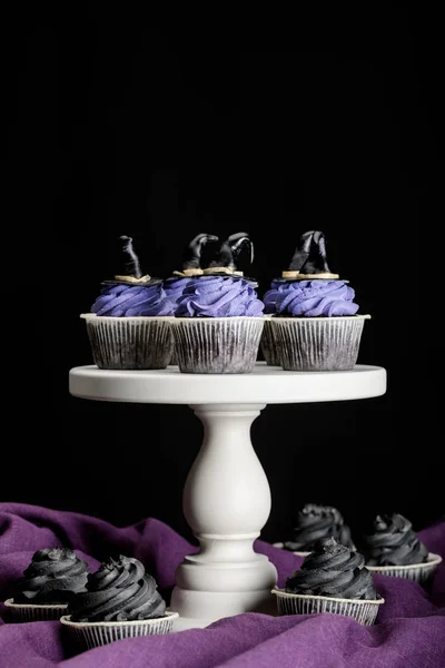 Saborosos cupcakes de Halloween no suporte branco em pano roxo isolado no preto — Fotografia de Stock