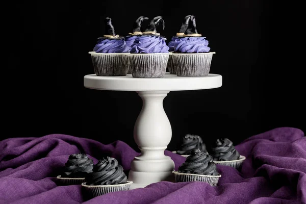 Sabrosos cupcakes de Halloween en soporte blanco en paño púrpura aislado en negro - foto de stock