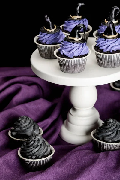 Sabrosos cupcakes de Halloween en soporte blanco en paño púrpura aislado en negro - foto de stock
