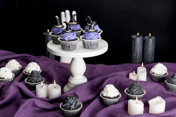 Tasty Halloween cupcakes on white stand near burning candles on purple cloth isolated on black — Stock Photo