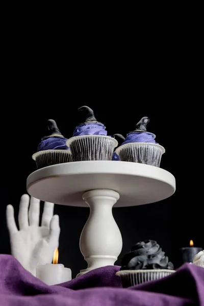 Visão de ângulo baixo de cupcakes de Halloween saborosos no suporte branco perto de velas em chamas em pano roxo isolado em preto — Fotografia de Stock