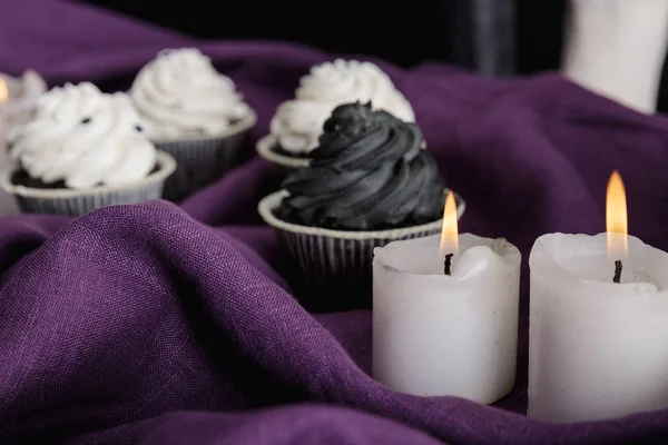 Selective focus of tasty Halloween cupcakes and burning candles on purple cloth — Stock Photo