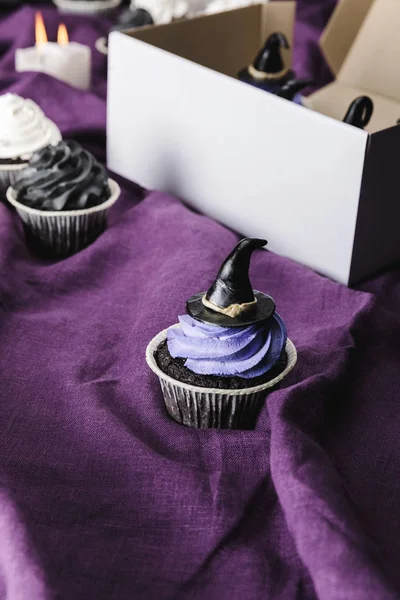 Смачний кекс на Хеллоуїн з блакитним кремом та декоративним капелюхом відьми на фіолетовій тканині — стокове фото
