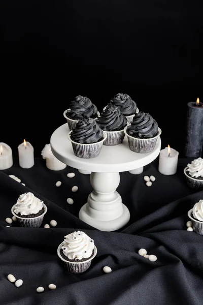 Sabrosos cupcakes de Halloween con crema negra en soporte blanco cerca de velas ardientes aisladas en negro - foto de stock