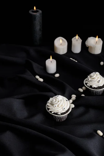 Смачні кекси на Хеллоуїн з білим кремом біля палаючих свічок на чорній тканині — стокове фото