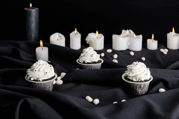 Tasty Halloween cupcakes with white cream near burning candles isolated on black — Stock Photo