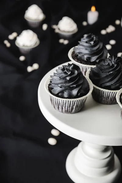Selektiver Fokus von leckeren Halloween-Cupcakes mit schwarzer Sahne am Stand in der Nähe brennender Kerzen — Stockfoto