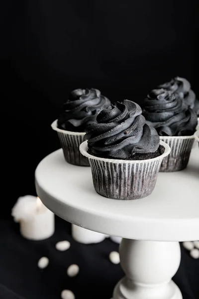 Savoureux cupcakes Halloween avec crème noire sur stand près de bougies brûlantes isolées sur noir — Photo de stock