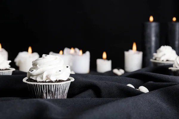 Selektiver Fokus von leckerem Halloween-Cupcake mit weißer Sahne in der Nähe brennender Kerzen isoliert auf schwarz — Stockfoto