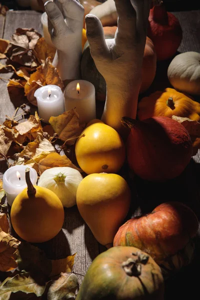 Сухая листва, горящие свечи, спелые тыквы и декоративные руки на деревянном деревенском столе — стоковое фото