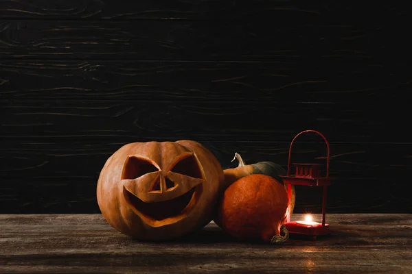 Calabaza de Halloween espeluznante tallada y vela ardiente sobre mesa rústica de madera sobre fondo negro — Stock Photo