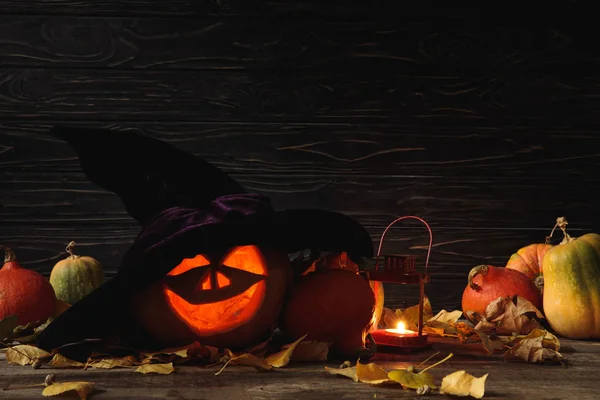 Citrouille d'Halloween fantasmagorique sculptée, feuilles automnales et bougie allumée sur table rustique en bois sur fond noir — Photo de stock