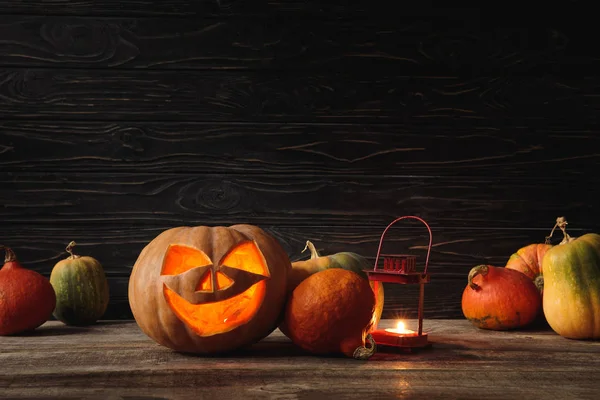 Carved spooky Halloween pumpkin and burning candle on wooden rustic table on black background — Stock Photo