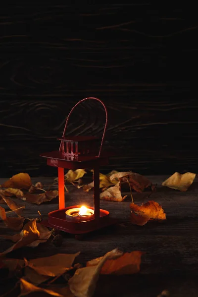 Hojas secas otoñales y vela encendida sobre mesa rústica de madera sobre fondo negro - foto de stock