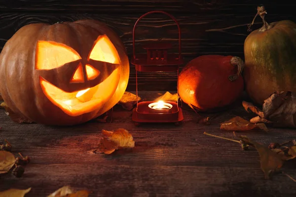 Zucca di Halloween spettrale intagliato, foglie autunnali e candela ardente su tavolo rustico in legno — Foto stock