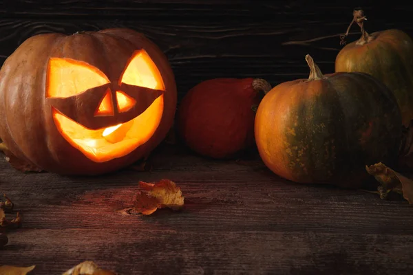 Zucca di Halloween spettrale intagliato, foglie autunnali e candela ardente su tavolo rustico in legno — Foto stock