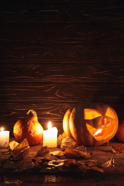 Zucca di Halloween spettrale intagliato, foglie autunnali e candele ardenti su tavolo rustico in legno — Foto stock