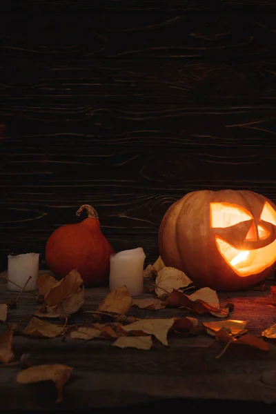 Gruseliger Halloween-Kürbis, herbstliche Blätter und Kerzen auf rustikalem Holztisch — Stockfoto