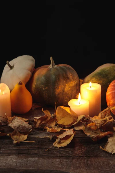 Сухе листя, палаючі свічки, стиглий гарбуз на дерев'яному сільському столі ізольовані на чорному — стокове фото