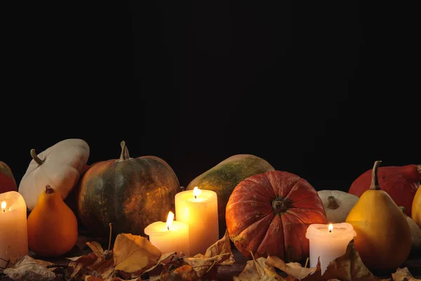 Feuillage sec, bougies allumées, citrouilles mûres sur table rustique en bois isolé sur noir — Photo de stock