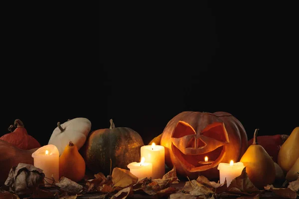 Feuillage sec, bougies allumées et citrouille sculptée Halloween sur table rustique en bois isolé sur noir — Photo de stock