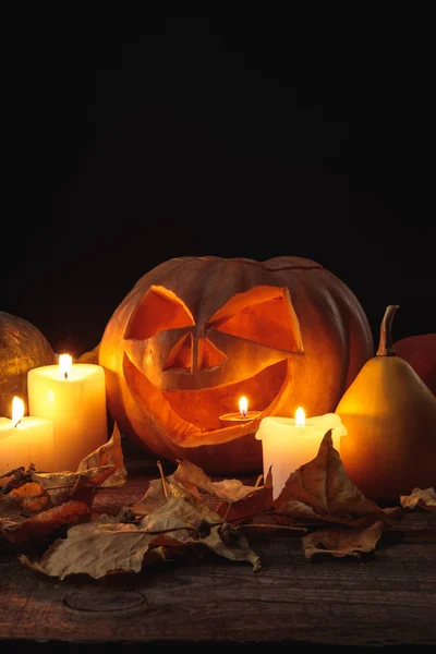 Feuillage sec, bougies allumées et citrouille sculptée Halloween sur table rustique en bois isolé sur noir — Photo de stock