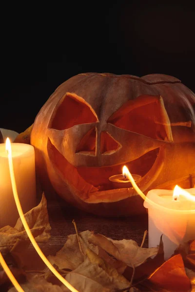 Folhagem seca, velas acesas e abóbora esculpida Halloween em mesa rústica de madeira isolada em preto — Fotografia de Stock