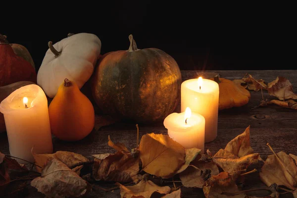 Follaje seco, velas encendidas, calabaza madura sobre mesa rústica de madera aislada en negro - foto de stock