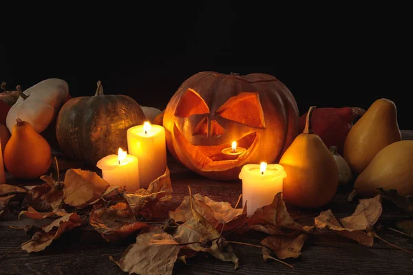 Сухая листва, горящие свечи и вырезанная на Хэллоуин тыква на деревянном деревенском столе, изолированном на черном — стоковое фото