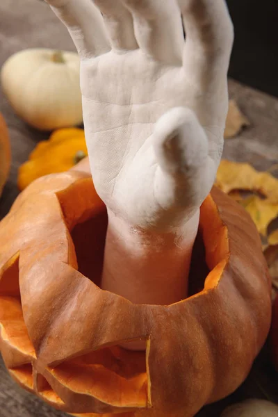Dekorative Hand in geschnitztem Halloween-Kürbis auf rustikalem Holztisch — Stockfoto