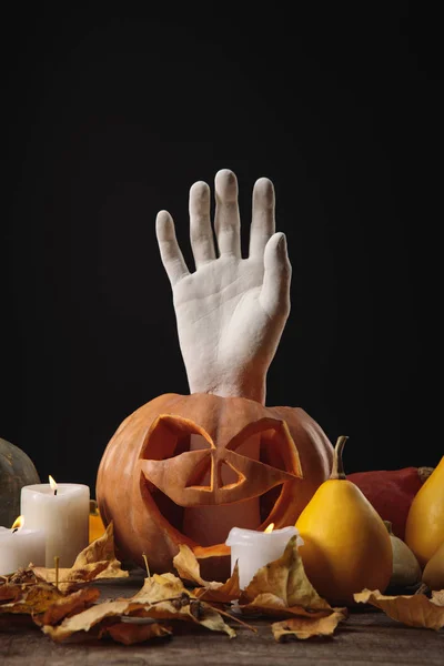 Folhagem seca, velas em chamas, mão decorativa em abóbora de Halloween esculpida em mesa rústica de madeira isolada em preto — Fotografia de Stock