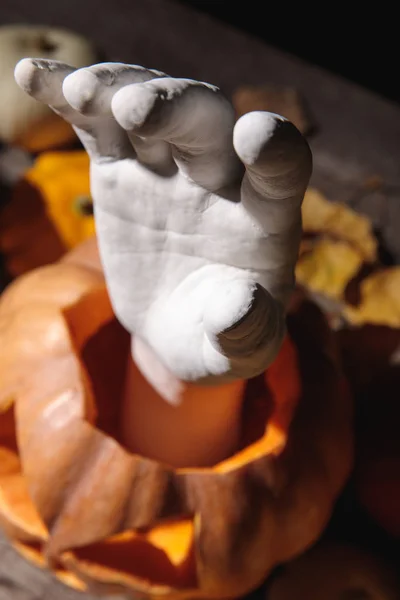 Selective focus of decorative hand in carved Halloween pumpkin on wooden rustic table — Stock Photo