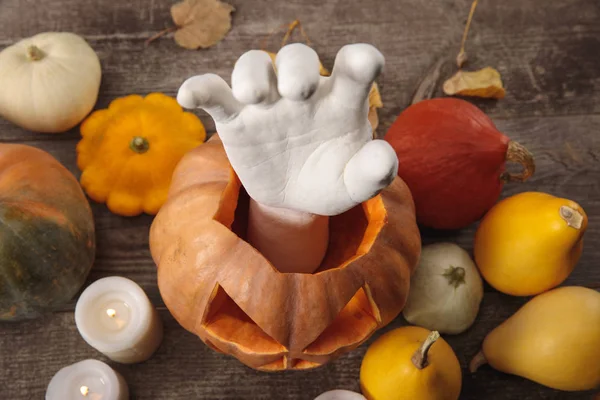 Top view of dry foliage, candles, decorative hand in carved Halloween pumpkin on wooden rustic table — Stock Photo