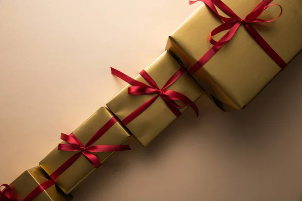 Acostado plano con cajas de regalo de oro con cintas rojas y arcos sobre fondo beige - foto de stock