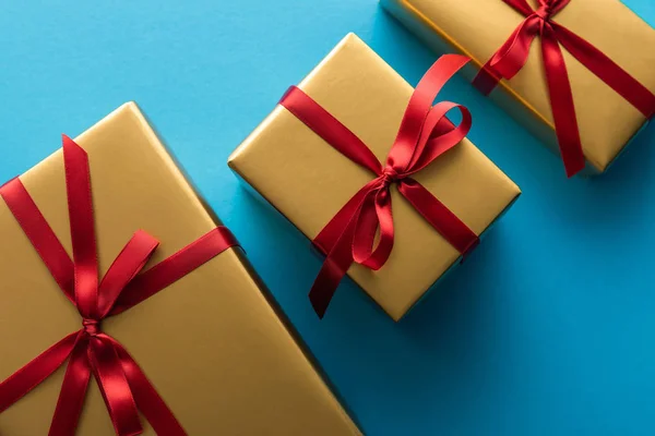 Вид зверху на золоті подарункові коробки з червоними стрічками та бантами на синьому фоні — стокове фото