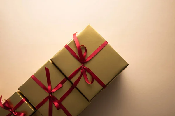 Вид зверху на золоті подарункові коробки з червоними стрічками та бантами на бежевому фоні — стокове фото
