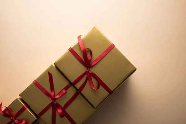 Top view of golden gift boxes with red ribbons and bows on beige background — Stock Photo