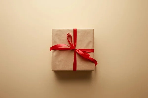 Top view of gift box in craft paper with red ribbon on beige background — Stock Photo