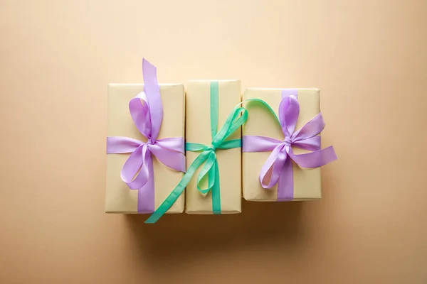Top view of gift boxes with violet and green ribbons on beige background — Stock Photo