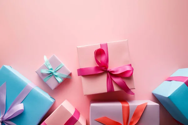 Blick von oben auf bunte Geschenkboxen mit Satinbändern auf rosa Hintergrund — Stockfoto