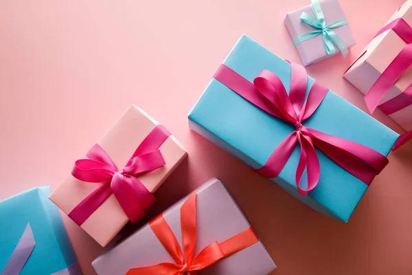 Blick von oben auf bunte Geschenkboxen mit Satinbändern auf rosa Hintergrund — Stockfoto