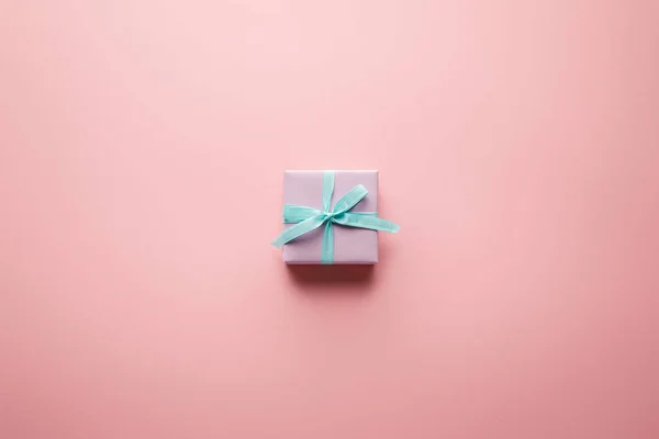 Вид зверху фіолетової маленької подарункової коробки з синьою атласною стрічкою на рожевому фоні — стокове фото