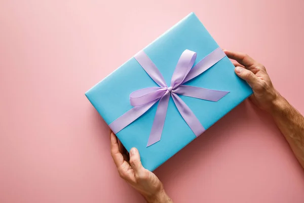 Vista recortada del hombre sosteniendo caja de regalo azul con cinta de satén violeta sobre fondo rosa — Stock Photo